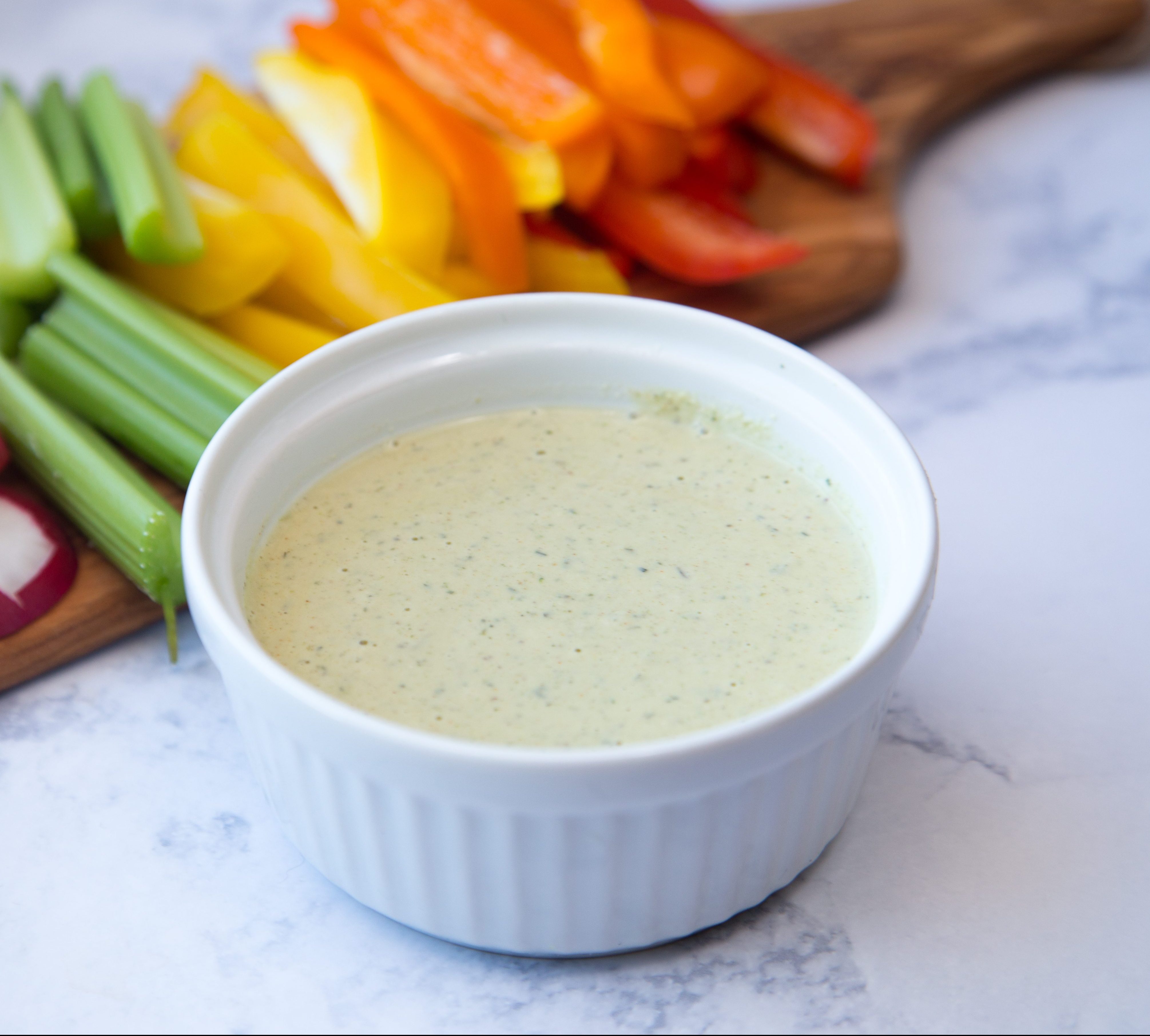 small ramekin of ranch dressing with sliced raw vegetables on a board in the background