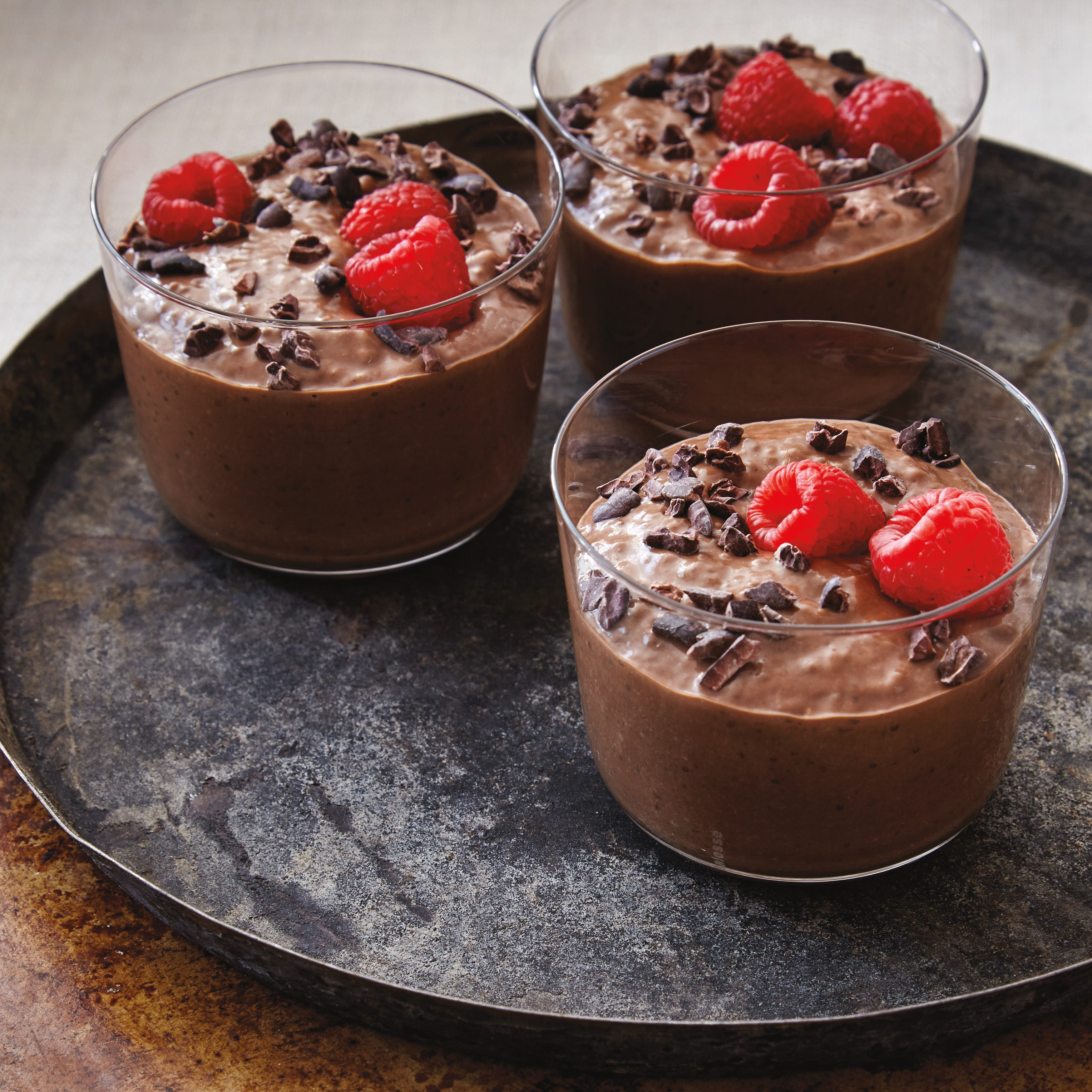 three small bowls of chocolate chia pudding topped with raspberries