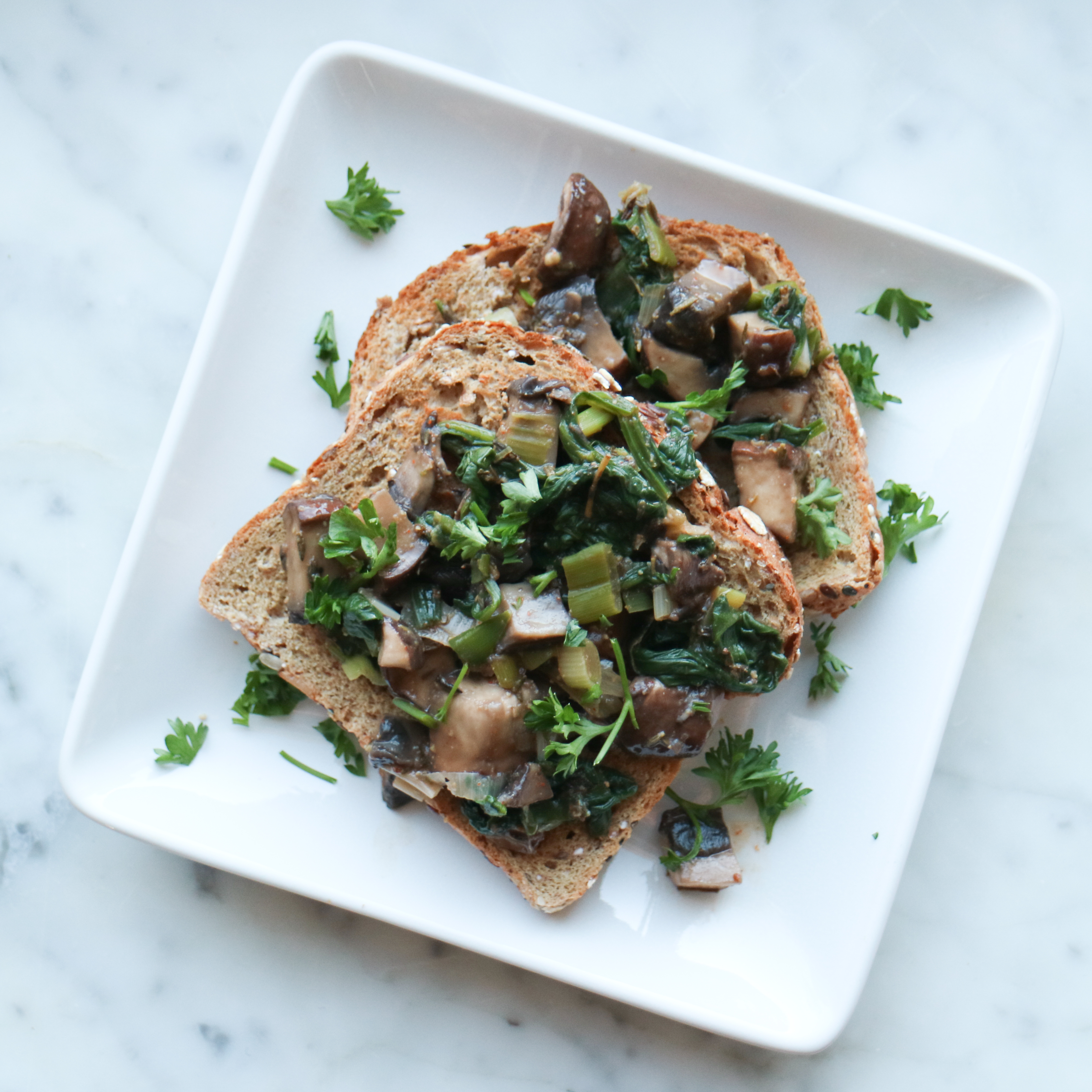 two slices of whole grain toast topped with mushrooms, spinach and parsley
