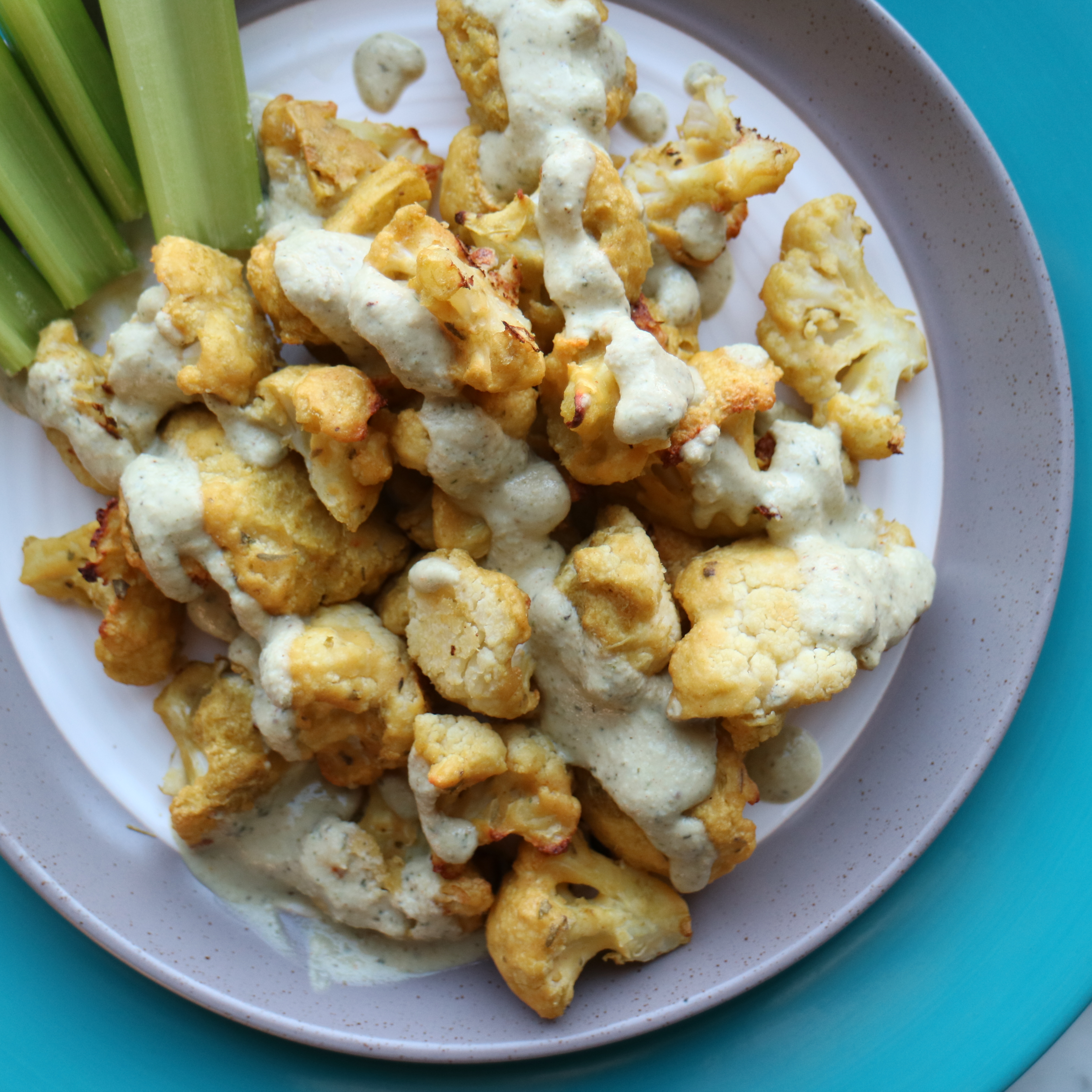 bowl of cauliflower wings drizzled with ranch sauce and a few ribs of celery