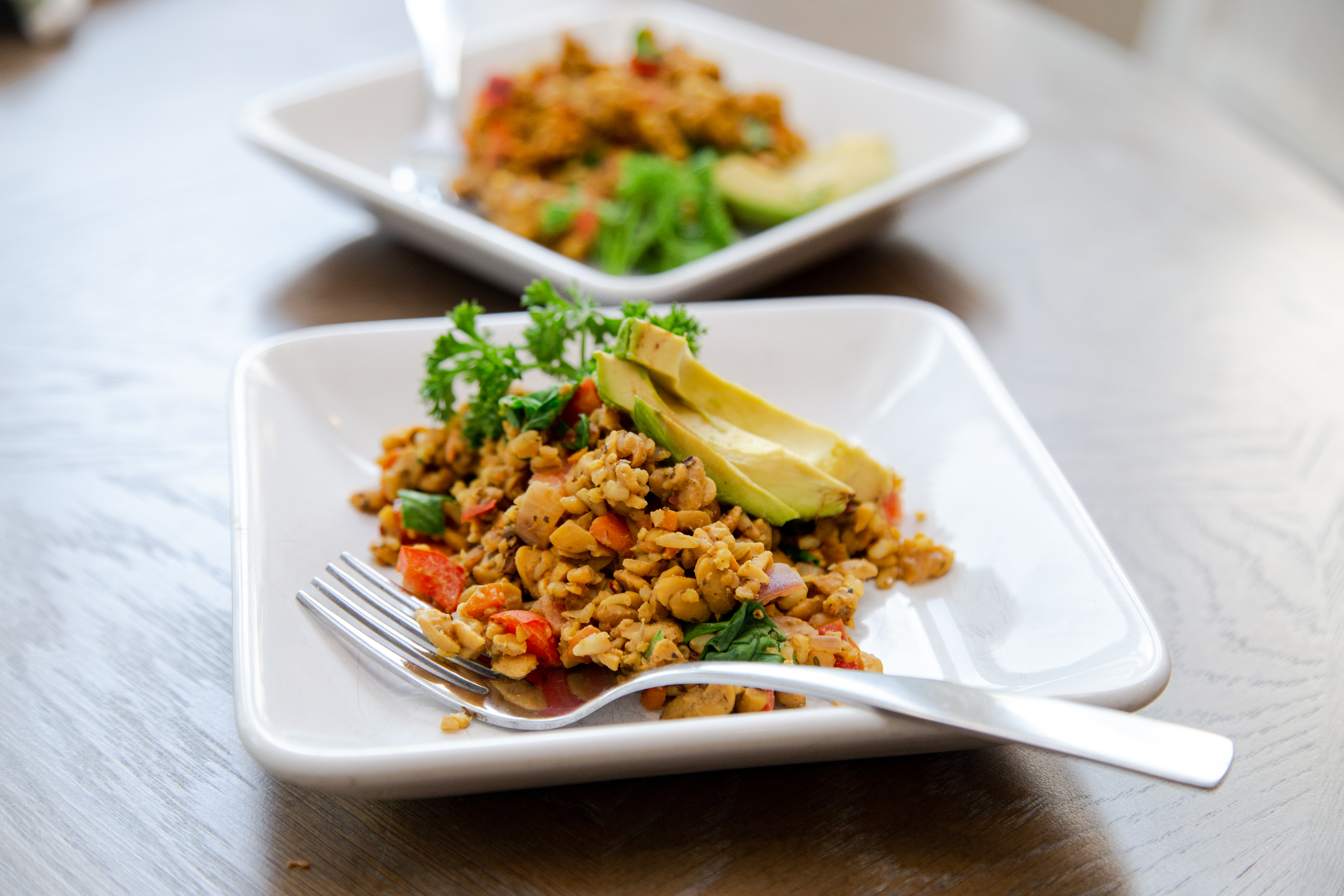 two dishes of tempeh scramble, sliced avocado, and parsley