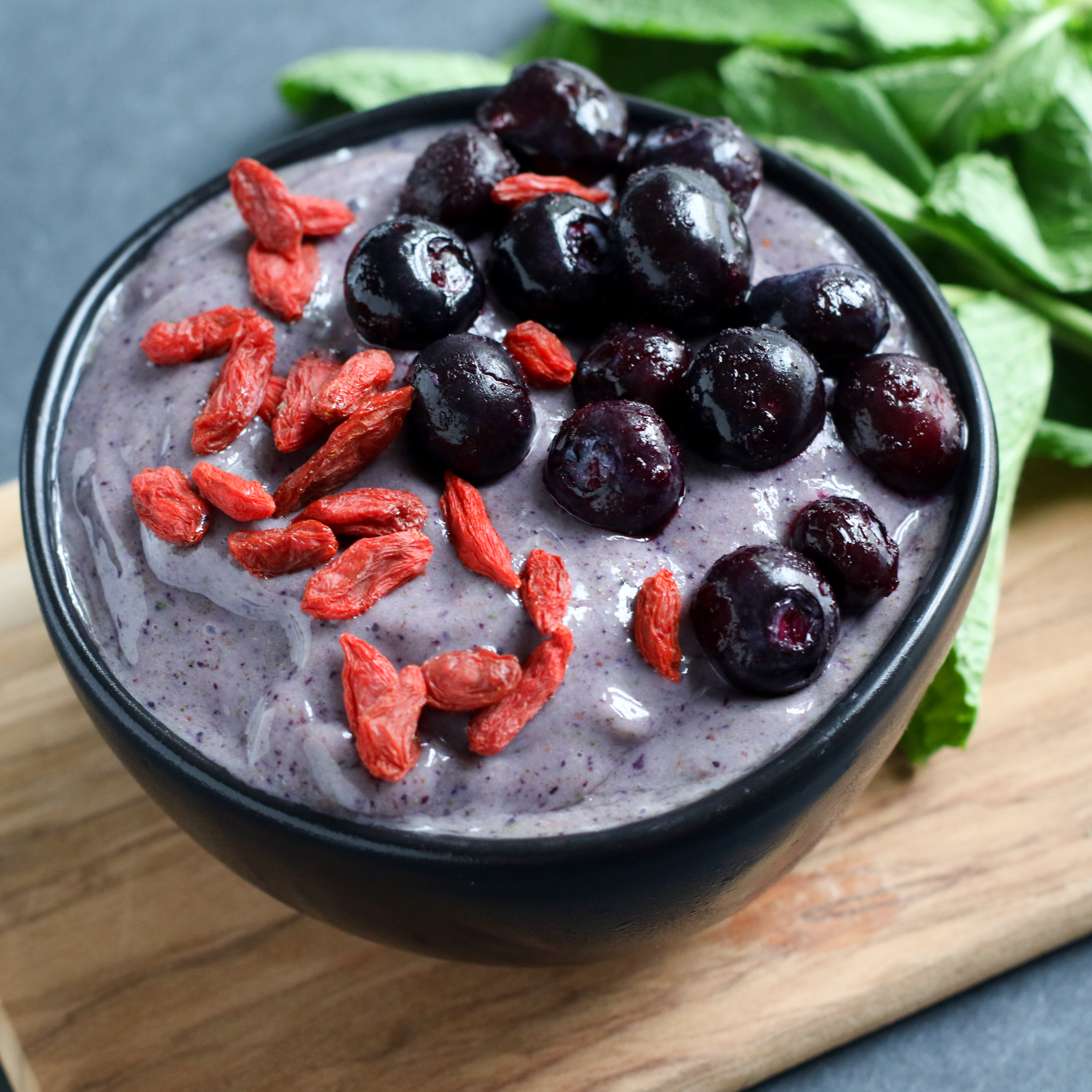 black bowl filled with mango berry nice creamed and topped with blueberries and goji berries