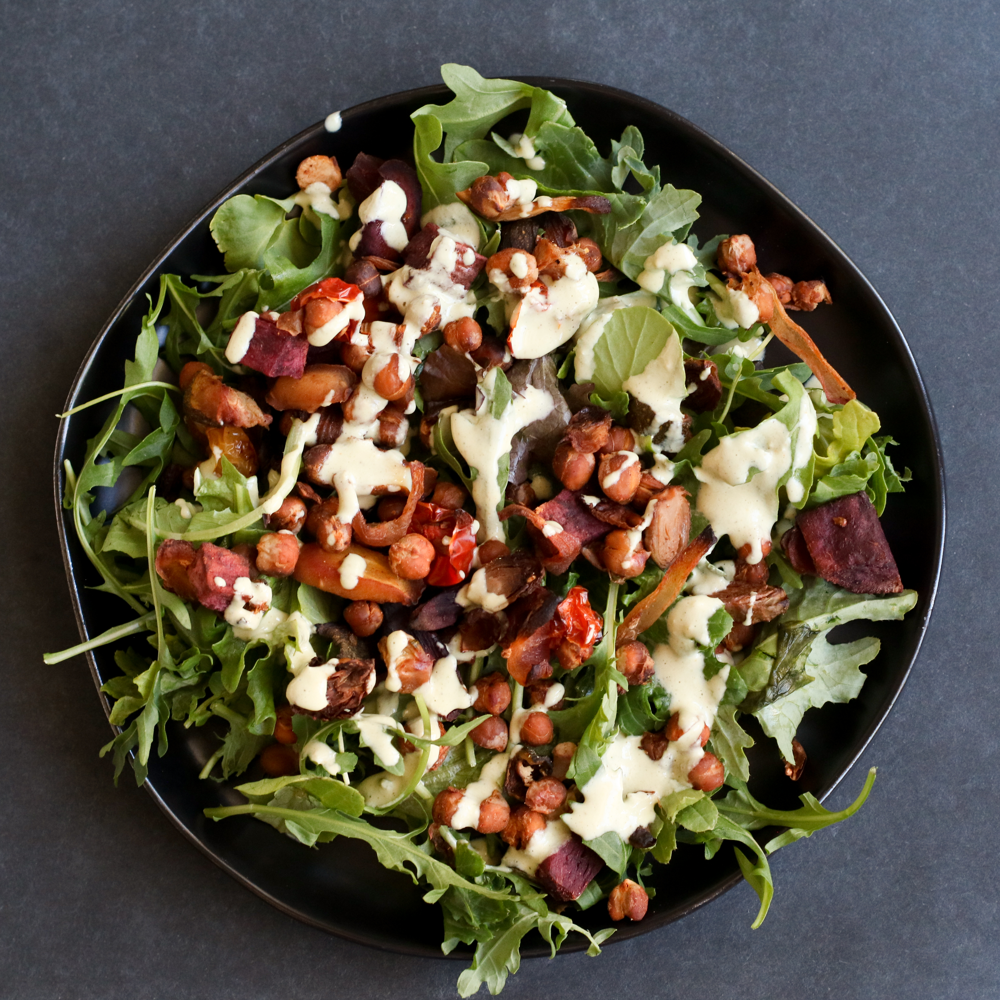 serving plate with greens, roasted vegetables and chickpeas, and sauce drizzled on top