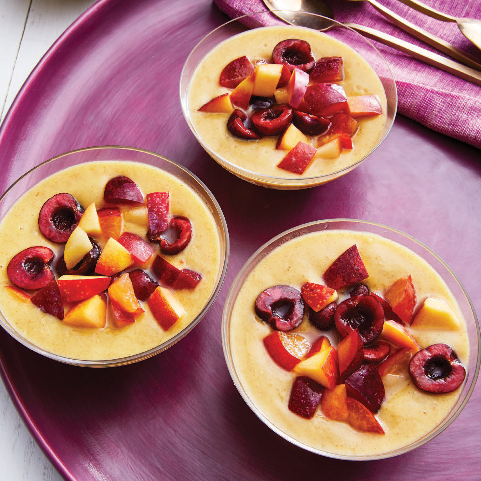 three bowls filled with mango smoothie and topped with sliced fruit