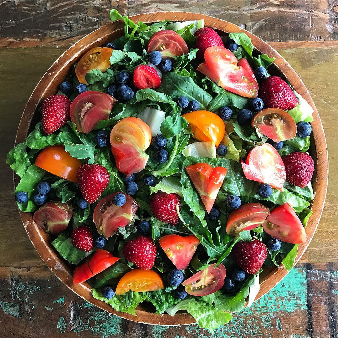 bowl filled with greens, berries, and tomatoes