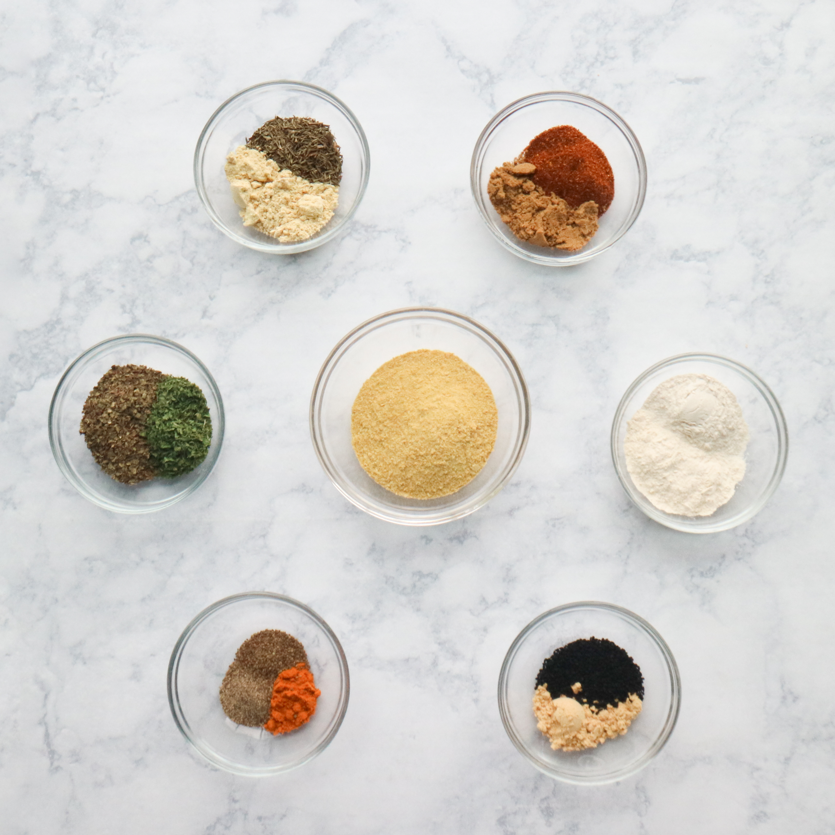seven small glass bowls filled with various herbs and spices