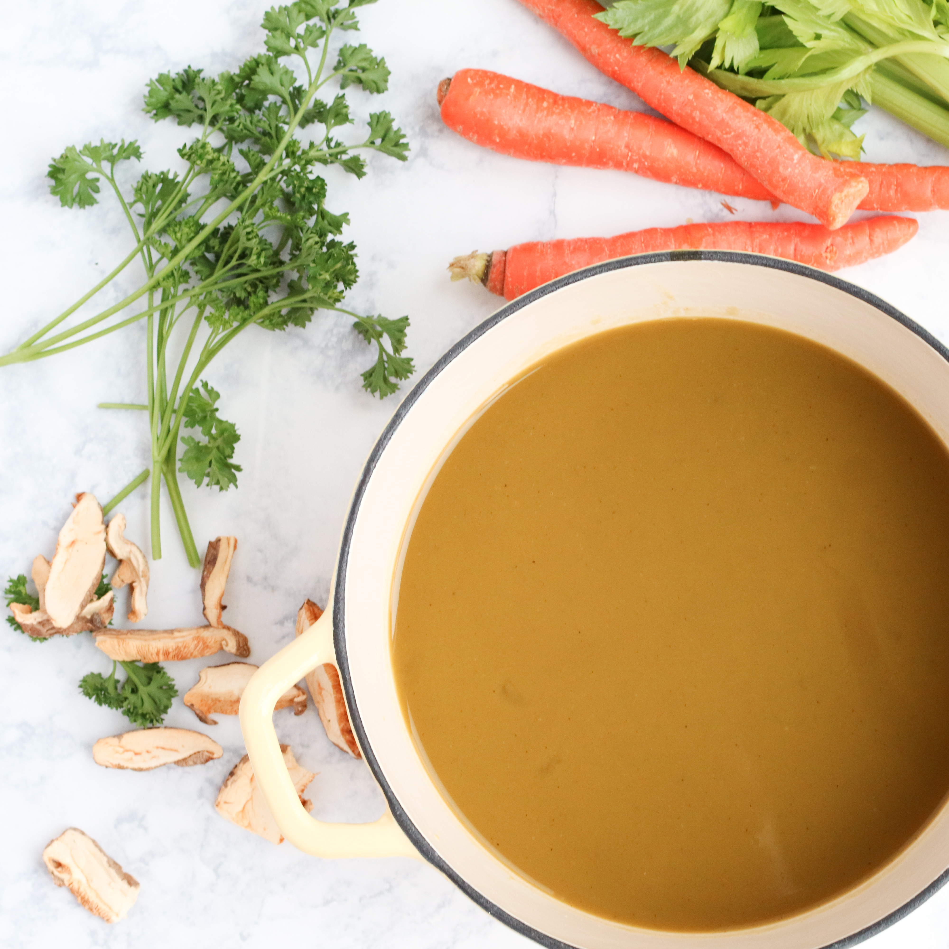 pot of vegetable broth, with vegetables and herbs in the background