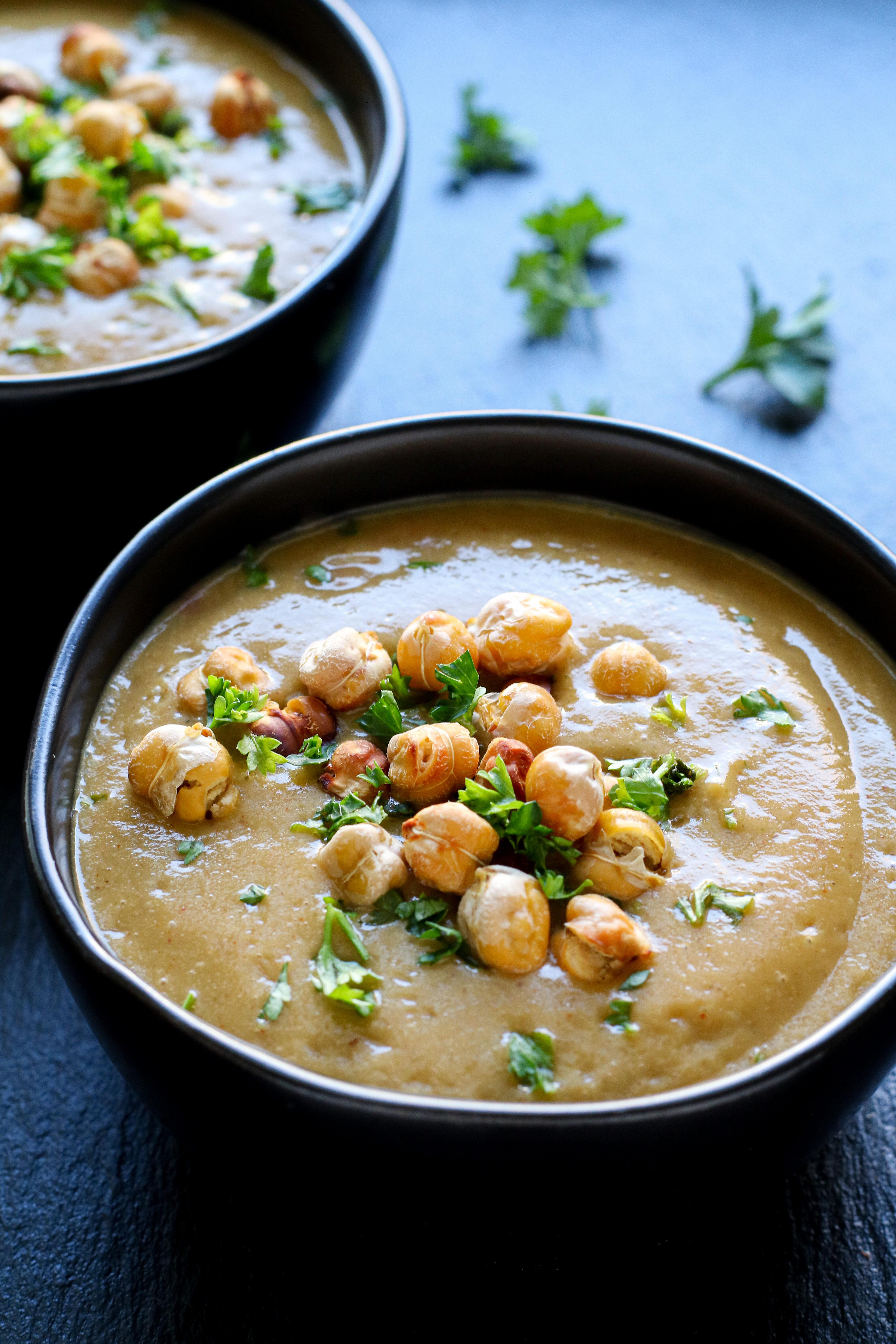 two bowls of cauliflower bisque topped with chickpeas and parsley